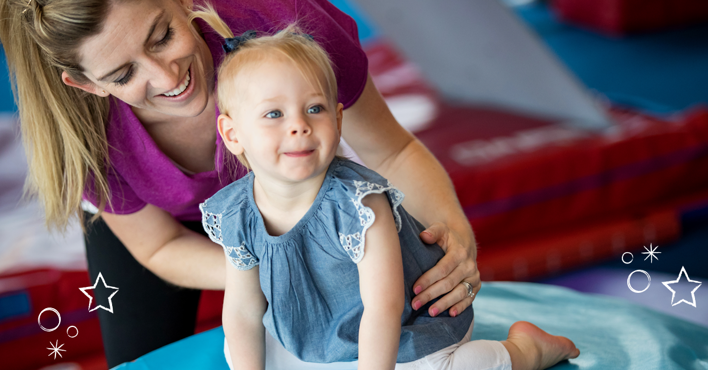 The Little Gym staff member holding a little girl on gym equipment