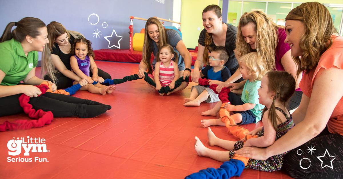 The Little Gym franchisees, parents and instructors sit in a circle with young children.